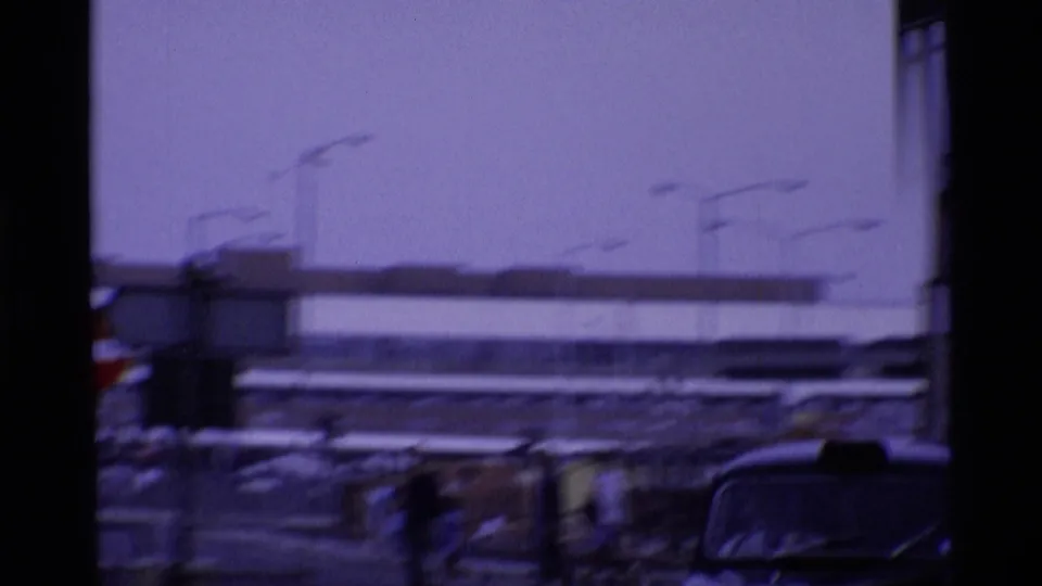 1969 London street view with motion-blurred cars, a broad modern building, and hazy blue-purple film color.