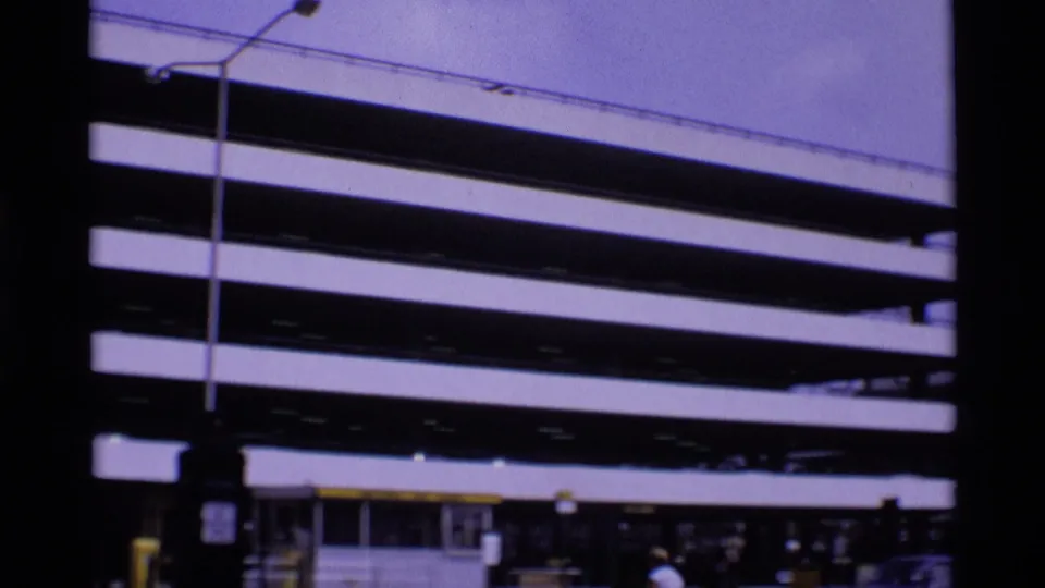 1969 London view of a striped multi-story parking deck, street lamps, and distant pedestrians near the base of the structure.