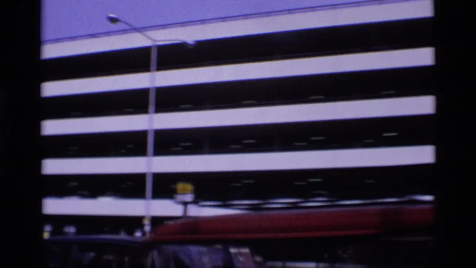 1969 London street frame with the striped parking deck in the background and a red car moving across the bottom of the shot.