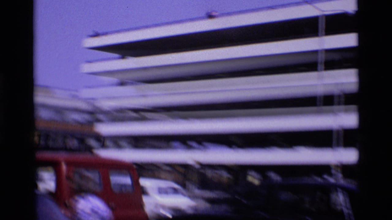 1969 London airport view of a multi-level parking structure, a red van, and parked cars seen in soft 8mm footage.