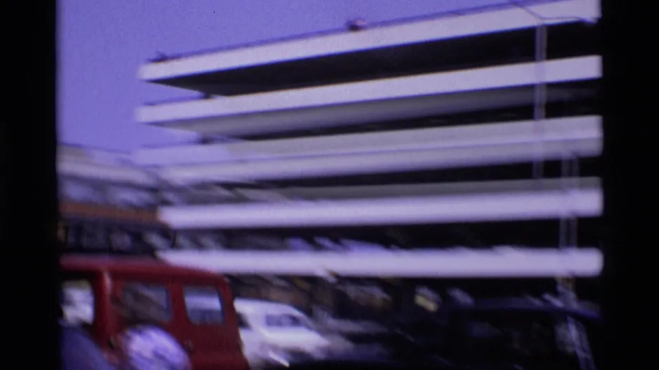 1969 London airport view of a multi-level parking structure, a red van, and parked cars seen in soft 8mm footage.
