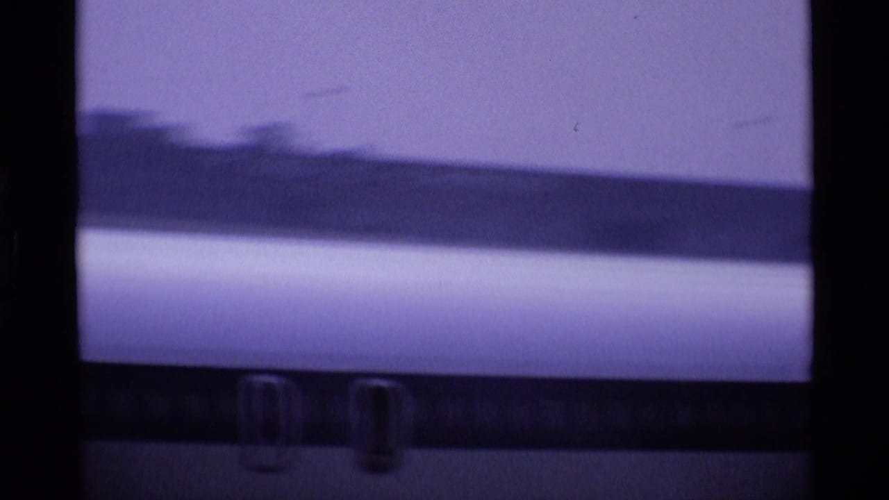 Soft 8mm frame from a London airport showing part of a jet fuselage with faint windows or markings through a hazy view.