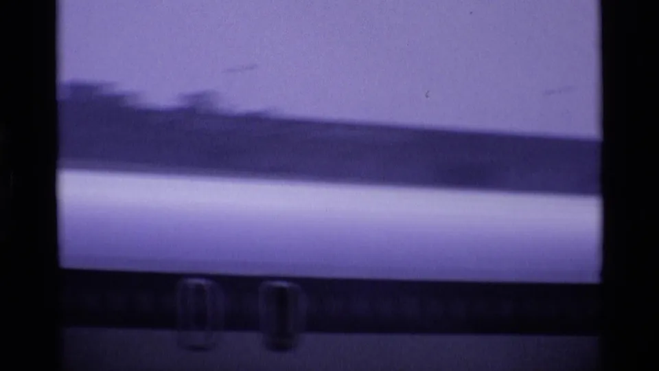 Soft 8mm frame from a London airport showing part of a jet fuselage with faint windows or markings through a hazy view.