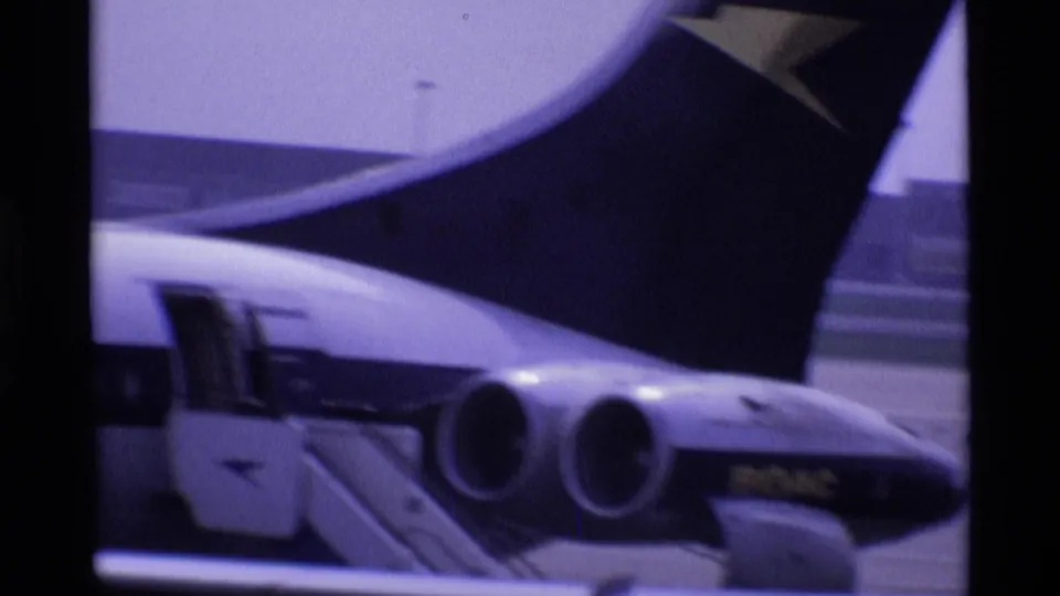 1969 London airport frame showing a jet tail, rear fuselage, and two visible engine nacelles near terminal structures.