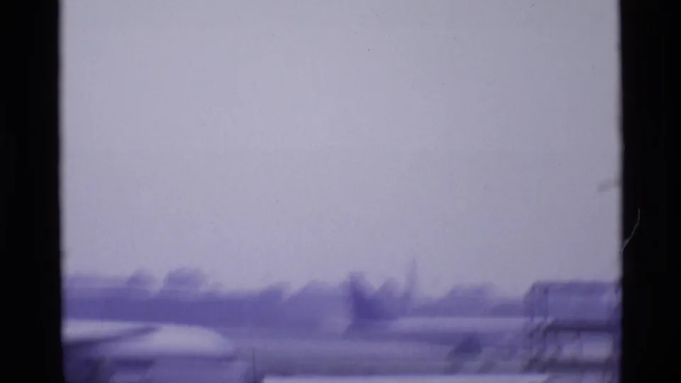 Hazy 1969 London airport view across a runway or apron, with distant structures and a partial aircraft edge in the foreground.