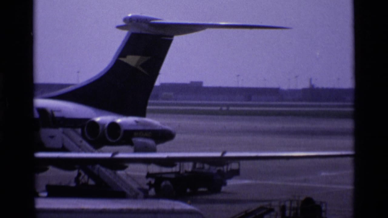 Parked aircraft tail seen through dark terminal window frames beside airport tarmac.