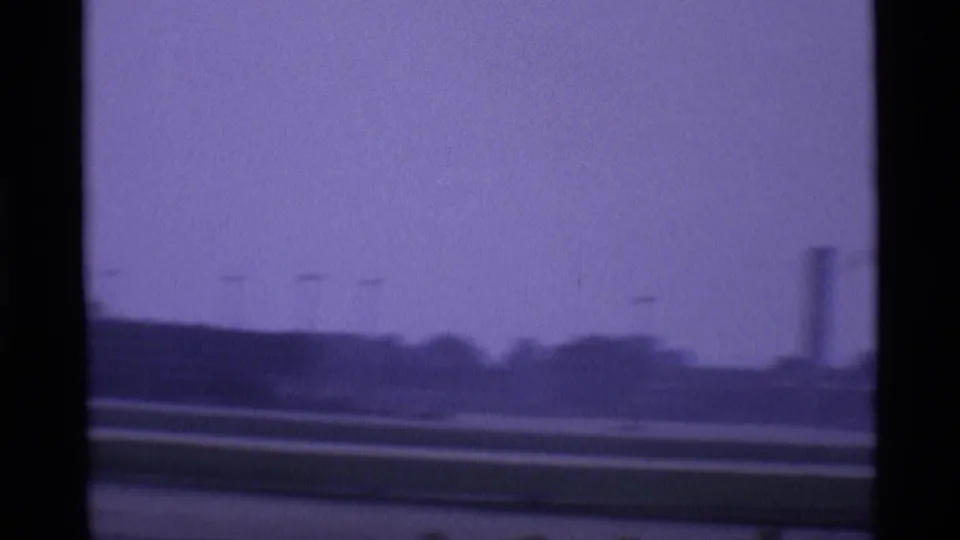 1969 London airport view across runway and distant airport structures, divided by dark terminal window framing.