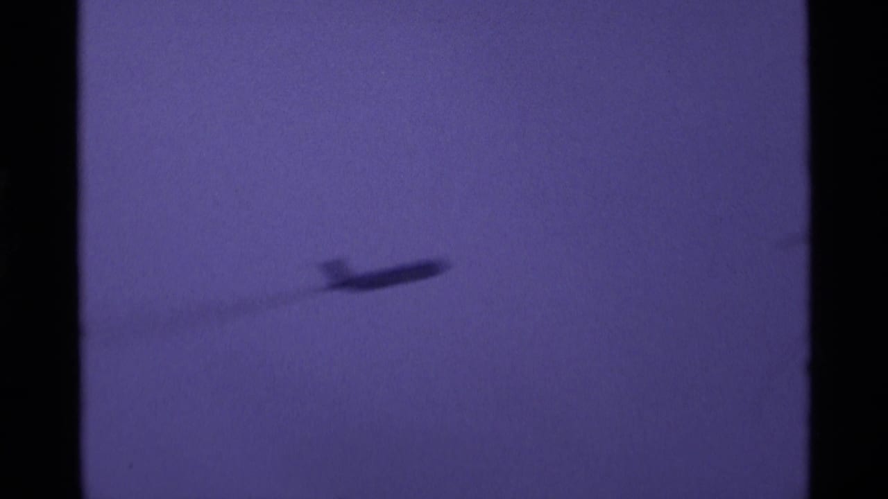 Small aircraft silhouette moving across an open purple sky.