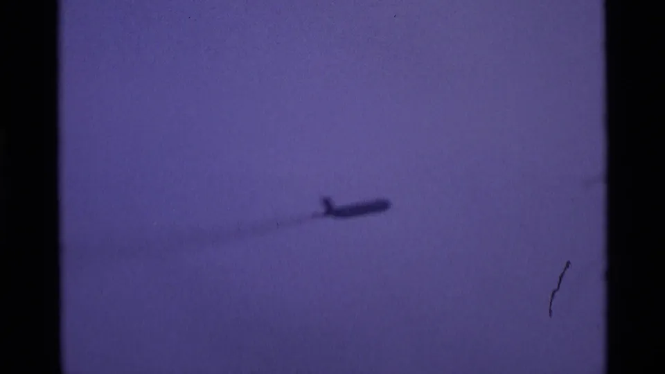 A distant plane passes through the lower purple sky, leaving a soft, diffuse trail or haze in the 1969 London 8mm footage.
