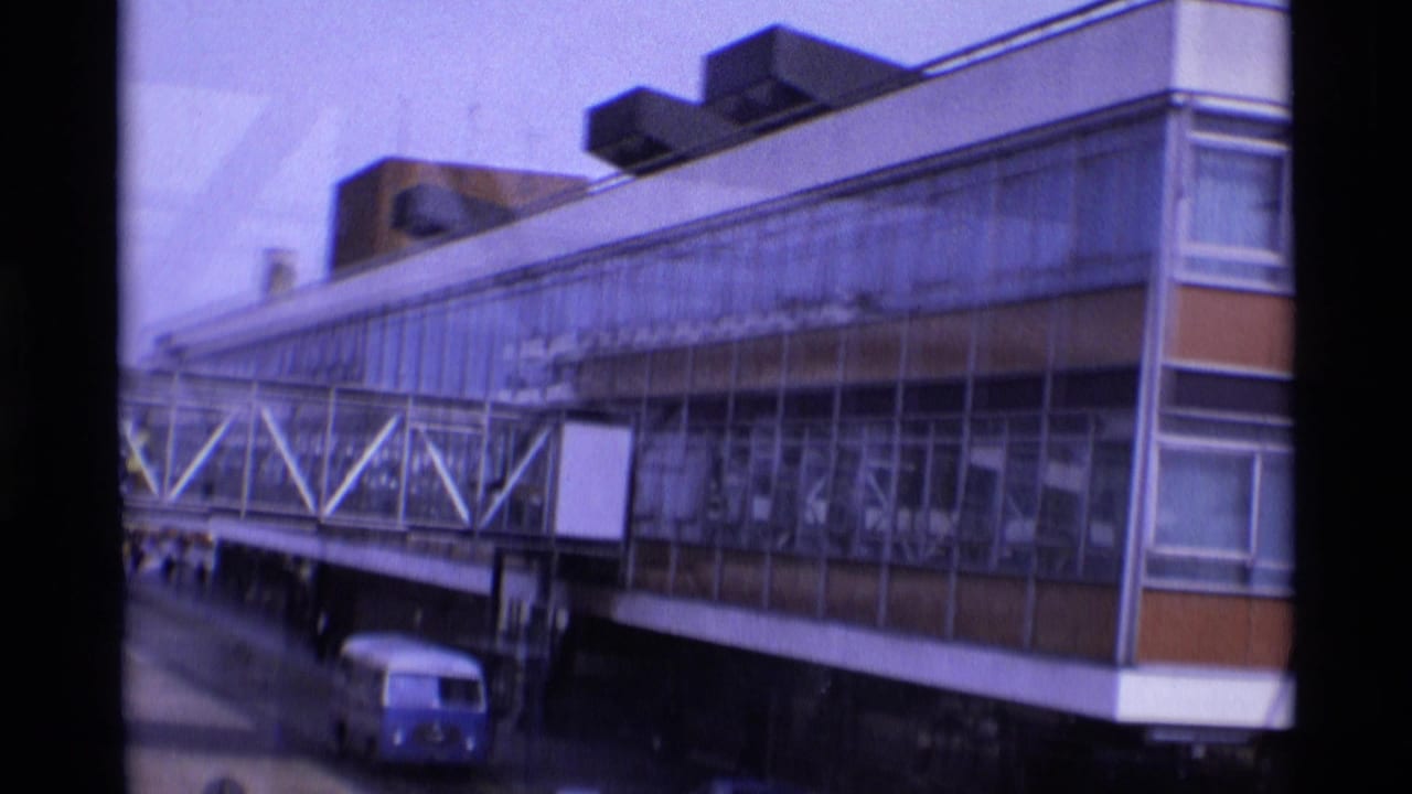 Airport terminal facade with enclosed bridge, blank sign panels, and a blue van below.