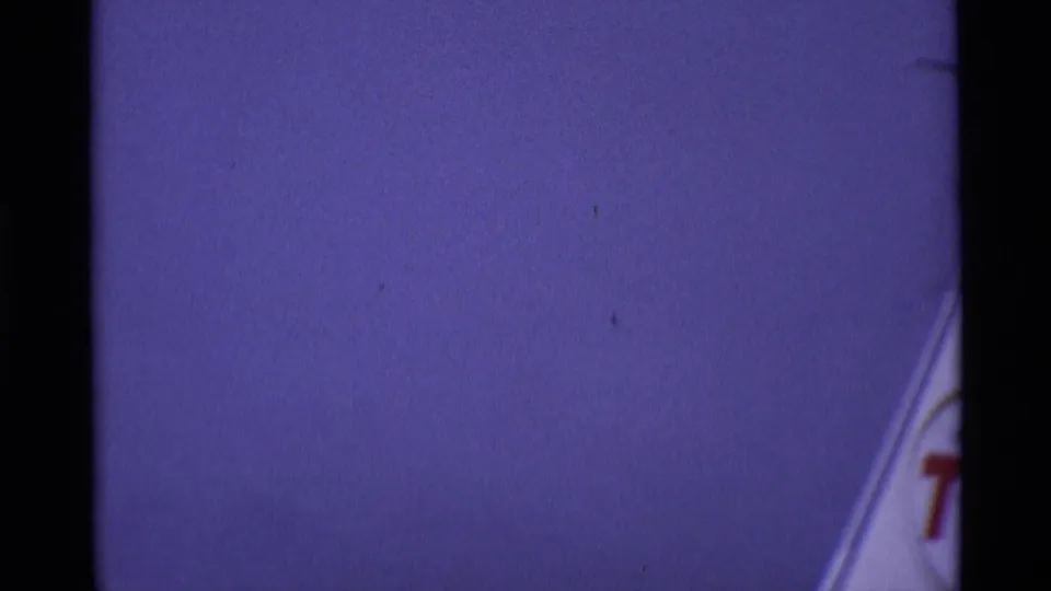 Partial aircraft tail detail in purple-shifted 8mm color, with red lettering only partly visible against the sky.