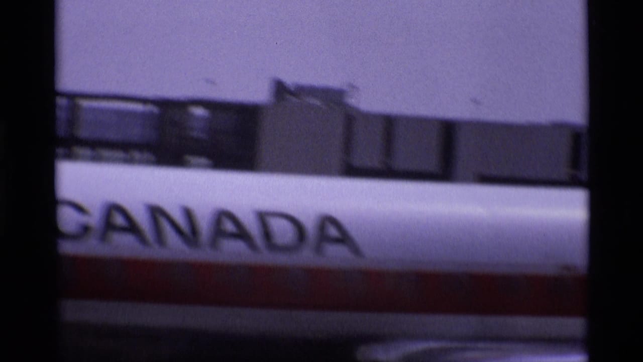 Canadian-marked aircraft fuselage at a London airport, with bold Canada lettering partly obscured by window framing.