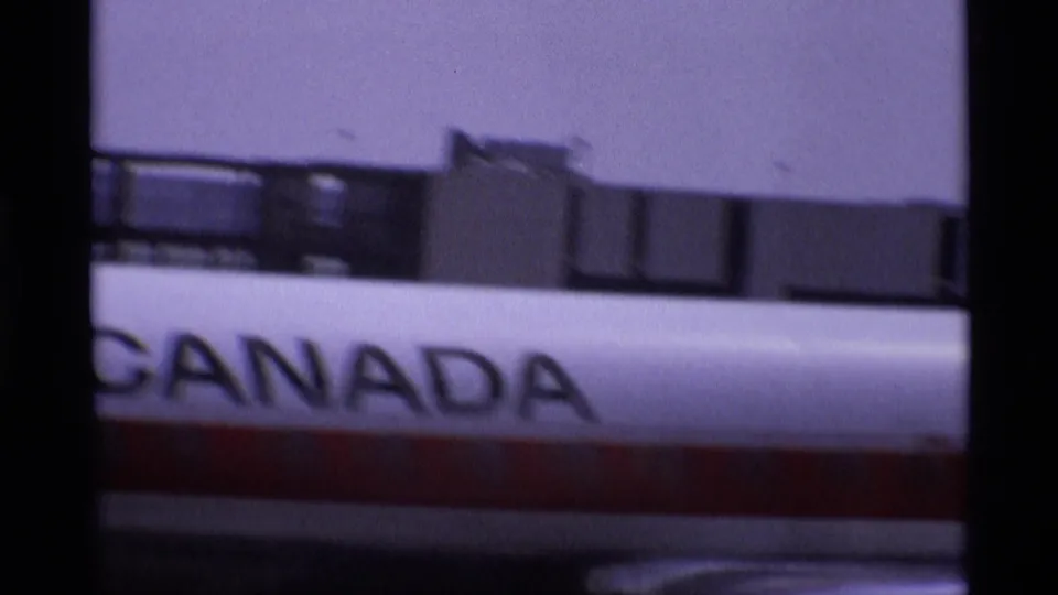 Canadian-marked aircraft fuselage at a London airport, with bold Canada lettering partly obscured by window framing.