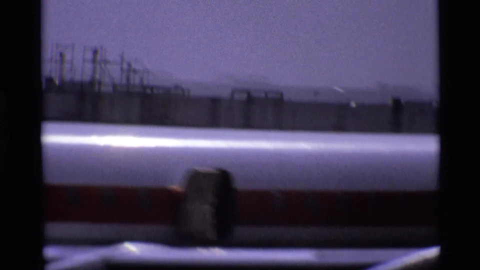 London airport view of a Canadian aircraft's lower fuselage and tarmac-side structures on grainy 8mm film.