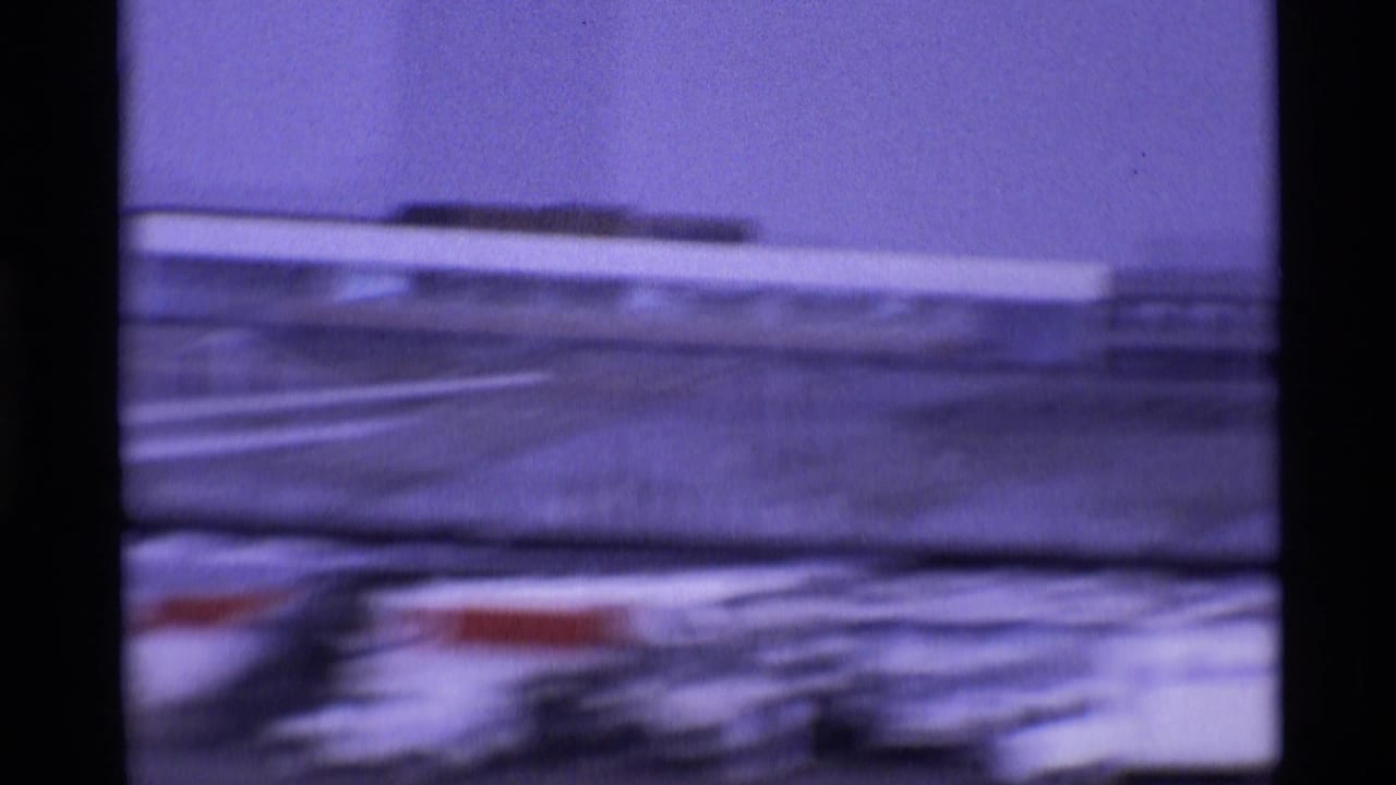 Shaky 1969 London airport home-movie frame showing blurred aircraft, apron markings, and distant terminal buildings.