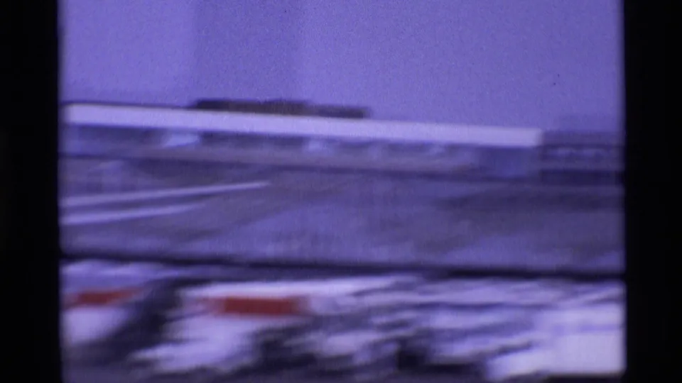 Shaky 1969 London airport home-movie frame showing blurred aircraft, apron markings, and distant terminal buildings.
