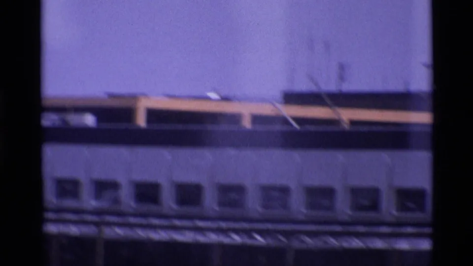 1969 London airport frame showing a terminal building facade, rooftop structures, and a hazy purple-blue sky.