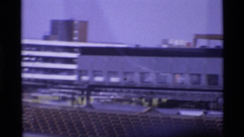 1969 London airport home-movie frame showing a multi-level terminal, windows, vehicles, and apron-side structures.