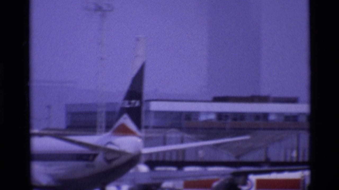 Delta-marked aircraft tail at a London airport in 1969, framed against terminal buildings and apron equipment.