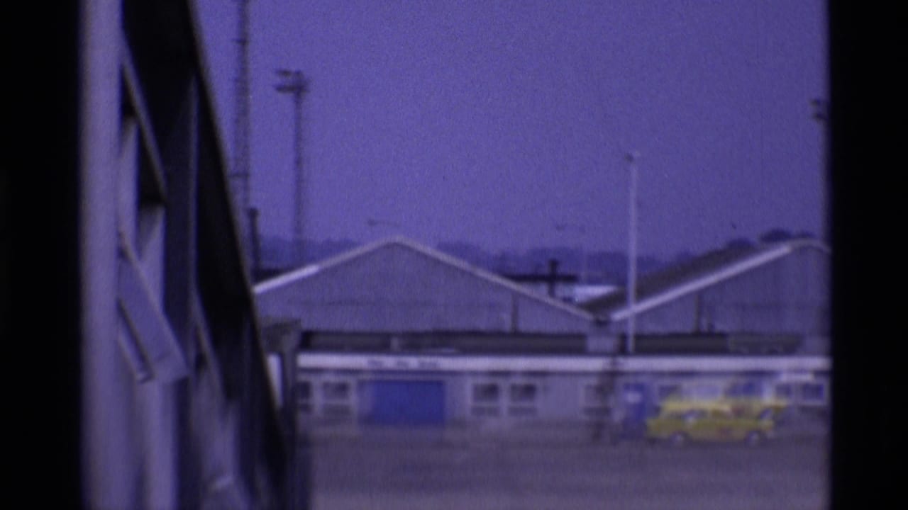 Terminal buildings seen through dark window framing with a yellow vehicle near blue doors.