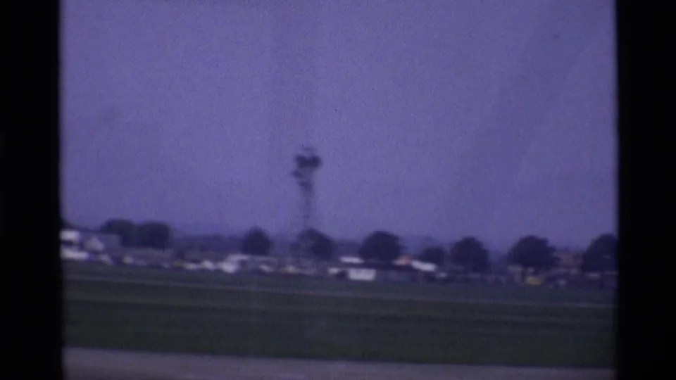 1969 London airport airfield view with grass, distant low buildings, and a tower-like structure beyond the tarmac.