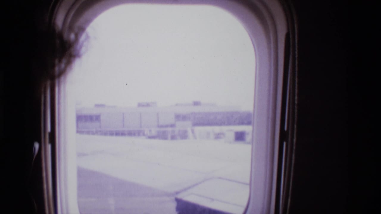 Aircraft window view of airport terminal and tarmac with dark cabin interior at left.