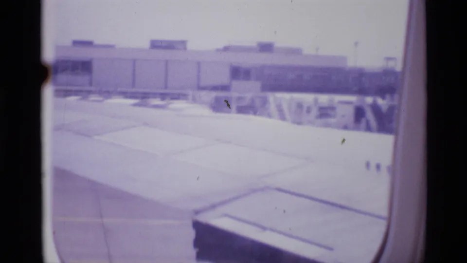 London airport terminal and tarmac viewed from inside a taxiing airplane in 1969 home-movie footage.