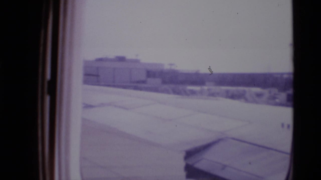 Aircraft wing beside a pale runway area with airport structures in the distance.
