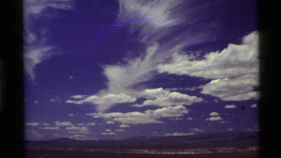 1972 8mm travel footage showing a broad Western sky with white clouds above distant low mountains and open land.