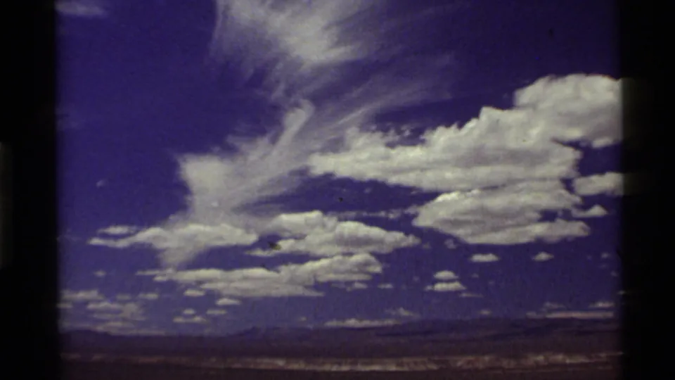 A 1972 home-movie view of billowing white clouds over open Western landscape, framed by dark 8mm film edges.