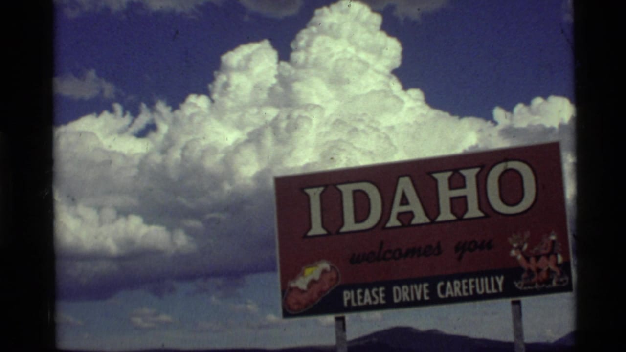 1972 8mm roadside view of an Idaho welcome sign against a dramatic cloud-filled sky near the Montana-Idaho travel route.