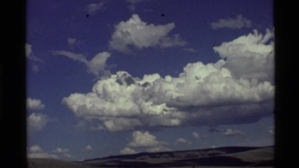 Final 8mm frame of the roadside cloudscape, with bright cumulus clouds over a low horizon in the 1972 travel footage.