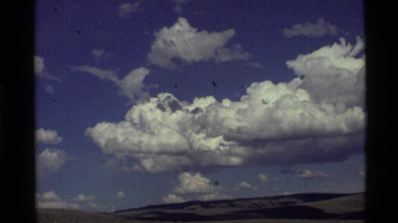 White cumulus clouds over a blue sky with a low dark horizon.