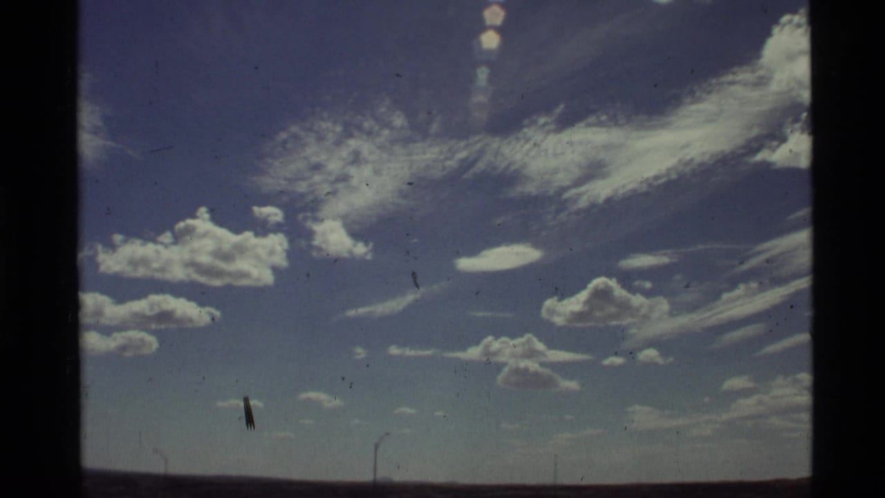 Blue sky with scattered clouds, low horizon, and visible 8mm film edges.