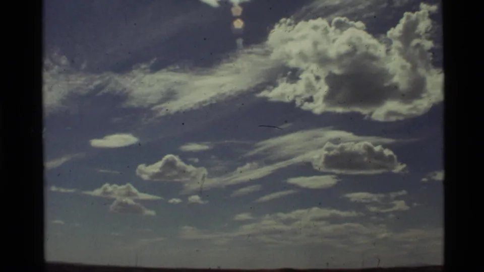 1972 Holland Lake, Montana frame with a large sunlit cloud, smaller lower clouds, thin cloud streaks, and visible 8mm grain.