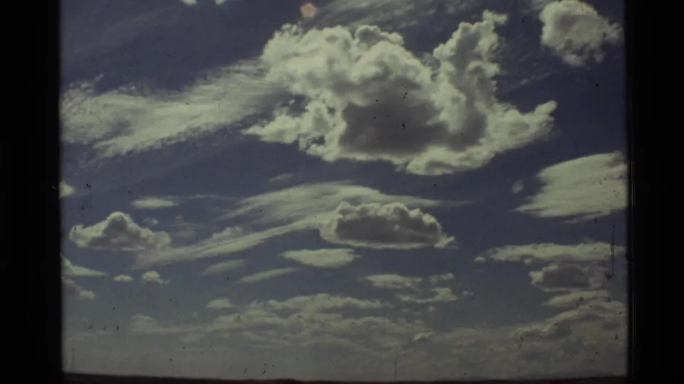 1972 Holland Lake, Montana home-movie frame showing layered clouds across a blue sky, low horizon, grain, and edge darkening.