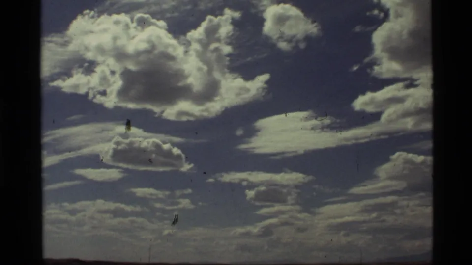 1972 Holland Lake, Montana 8mm frame with bright white clouds, layered sky texture, visible gate edges, and minor film dust.