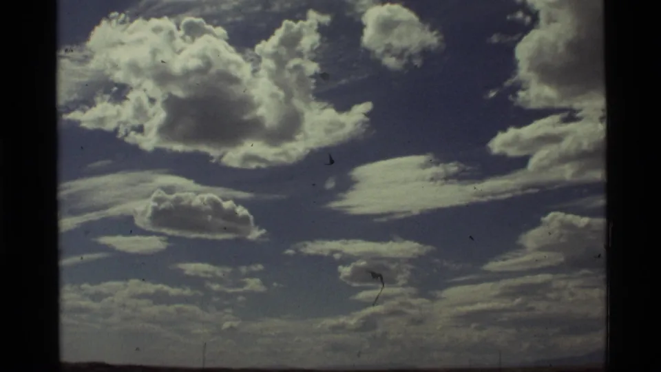 1972 Holland Lake, Montana 8mm frame showing a large sunlit cloud, smaller cloud forms, blue sky, and faint land or horizon below.
