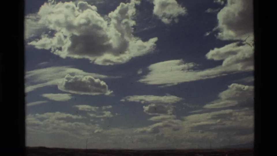 1972 Holland Lake, Montana 8mm frame with layered cumulus and wispy clouds over a faint horizon, with grain and gate edges visible.