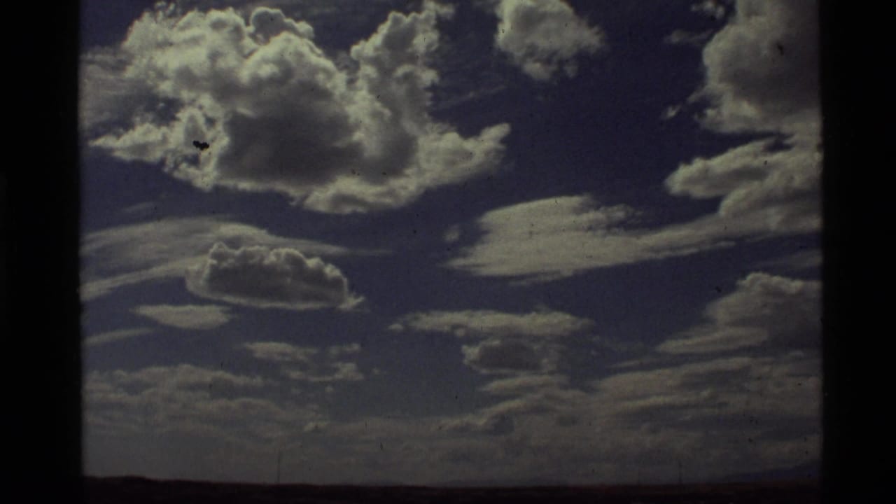 1972 8mm footage at Holland Lake, Montana, showing bright cumulus clouds against a deep blue sky with visible film grain and gate edges.