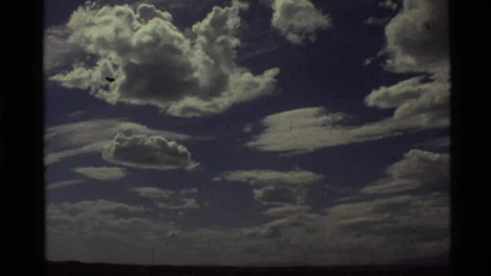 1972 8mm footage at Holland Lake, Montana, showing bright cumulus clouds against a deep blue sky with visible film grain and gate edges.