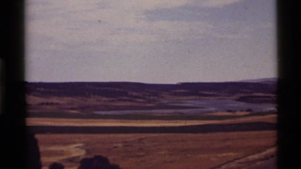 Final 1972 Holland Lake frame showing dry rolling fields, distant water, low hills, and a washed pale sky with 8mm color shift.