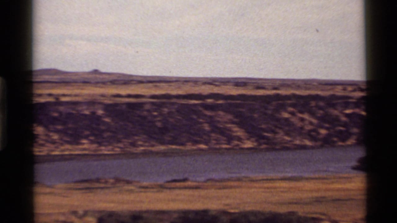 1972 8mm view near Holland Lake, Montana, with calm blue water, dry grassland, distant hills, and visible film gate edges.