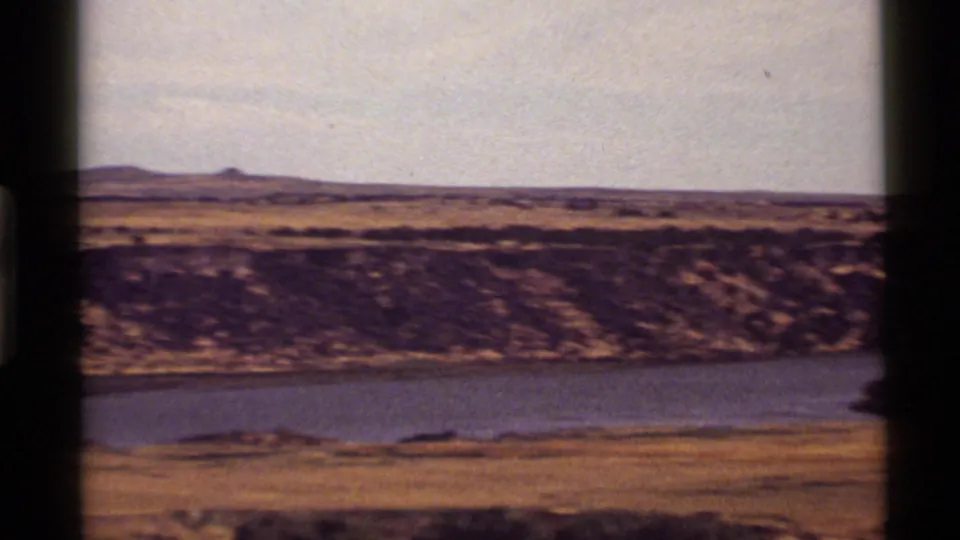 1972 8mm view near Holland Lake, Montana, with calm blue water, dry grassland, distant hills, and visible film gate edges.