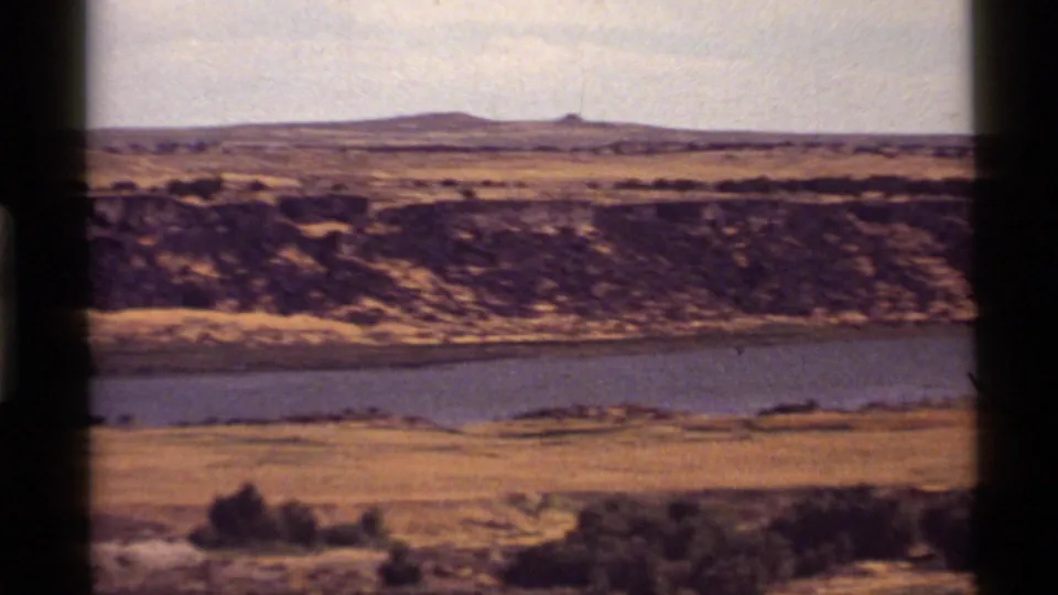 The pan continues across Holland Lake, Montana, showing a water channel, dry open ground, eroded banks, and low hills under a pale sky.