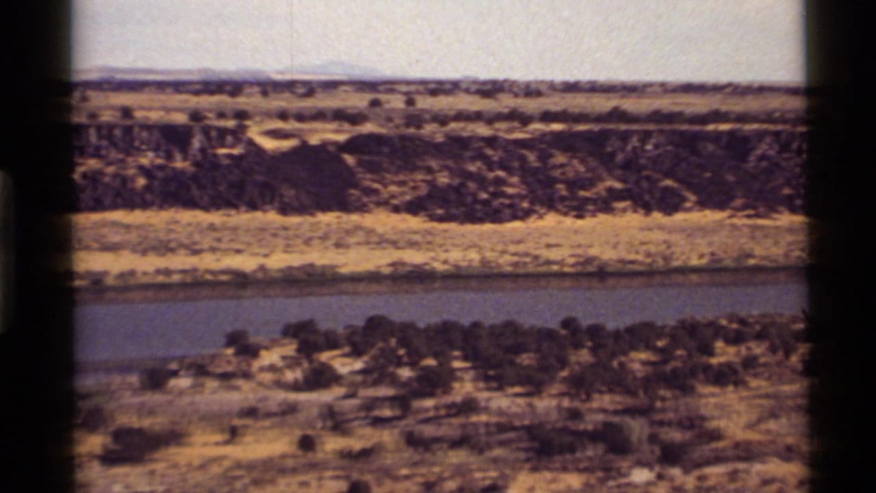 1972 8mm view near Holland Lake, Montana, showing a broad river below dry banks, sparse trees, and distant ridges.