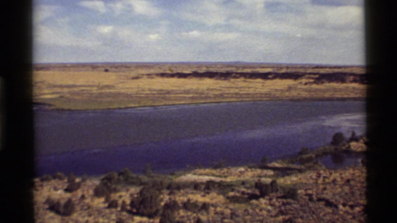 1972 8mm view near Holland Lake, Montana, showing blue water, golden fields, low shoreline, and a cloudy sky.
