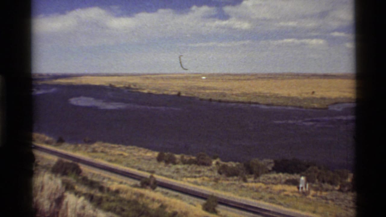 Waterway and highway crossing open country with dark film borders visible.
