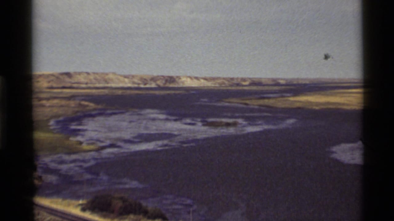 Zoomed 1972 Holland Lake view showing open water, marshy shoreline, distant pale hills, and faded 8mm color.