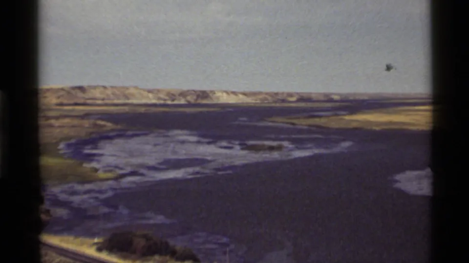 Zoomed 1972 Holland Lake view showing open water, marshy shoreline, distant pale hills, and faded 8mm color.